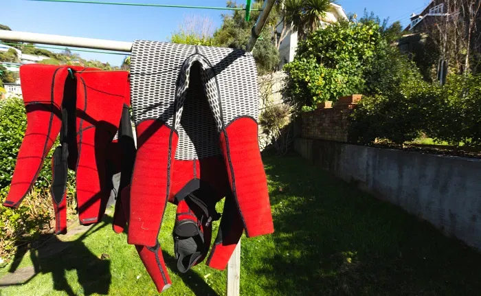 Chalecos y protecciones rojas para deportes acuáticos colgados al aire libre en un tendedero, con jardín y casa de fondo.