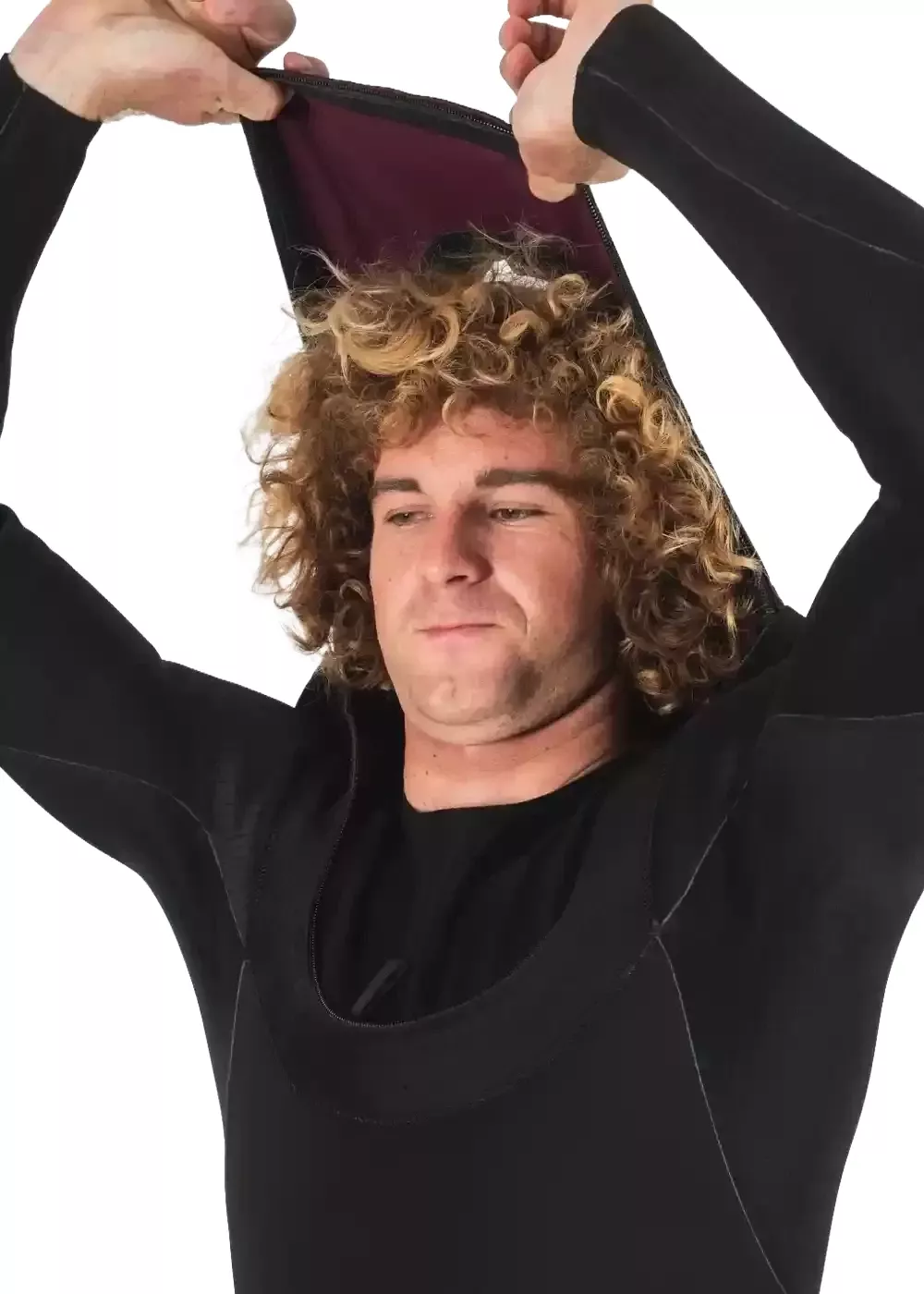 Homme en combinaison de surf noire ajustant l’ouverture autour du cou, regard concentré, cheveux blonds bouclés. Alt text pour produit de plongée/surf.