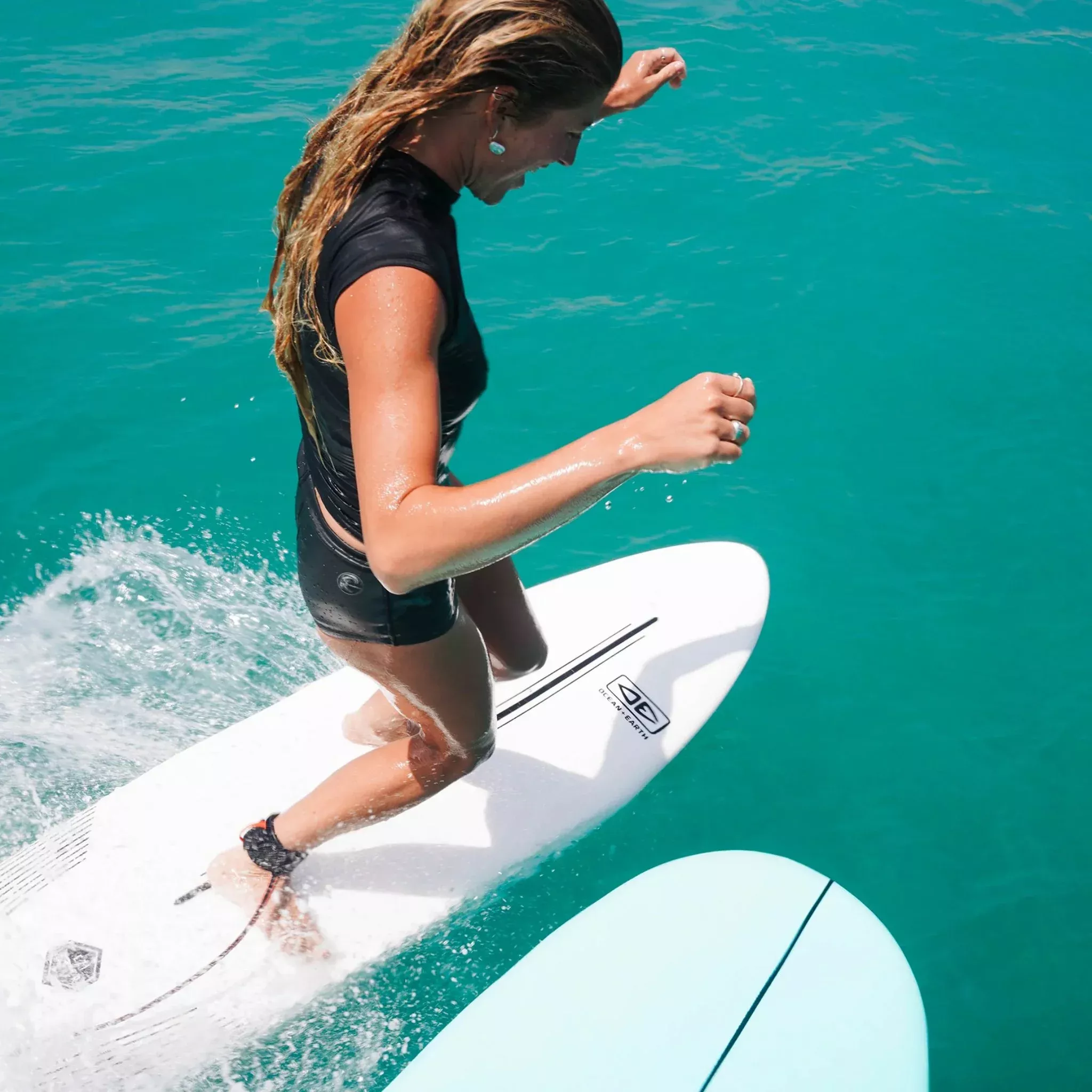Surfeuse en combinaison noire sur une planche de stand-up paddleboard dans une eau turquoise.