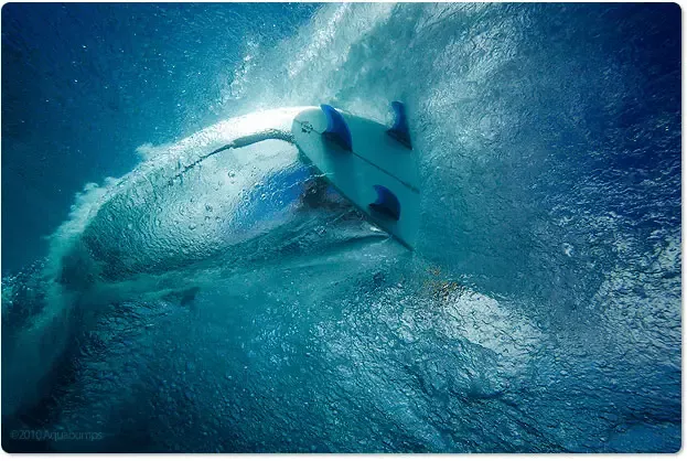 Tabla de surf curva dentro de una ola azul, rodeada de espuma y agua cristalina. Tabla de surf curva dentro de una ola azul, rodeada de espuma y agua cristalina.