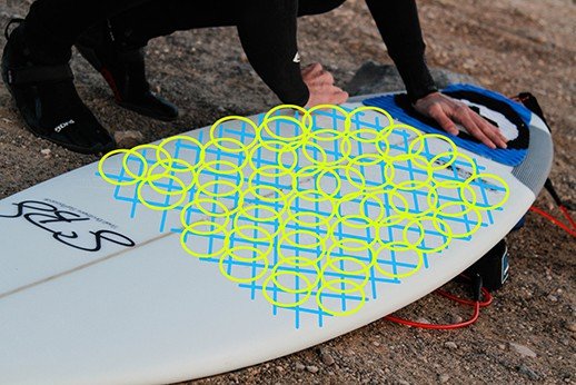 Tablero de surf con diseño de figuras geométricas en colores azul y amarillo, preparado para colocación de leash en entorno de playa.